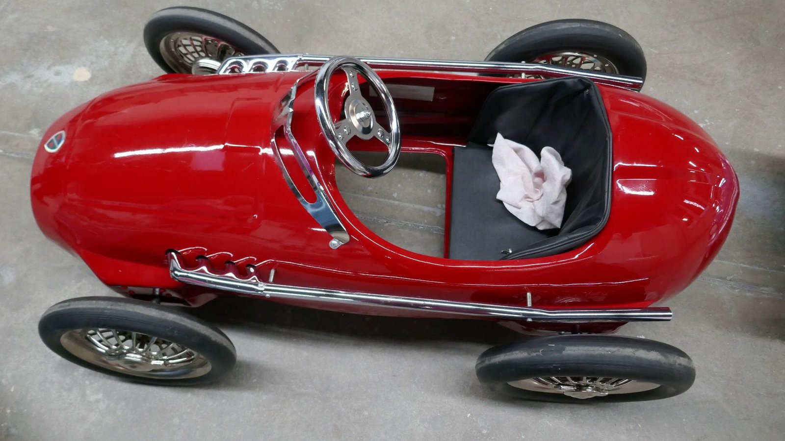 Ein rotes Tretauto mit schwarzem Sitz und Lenkrad